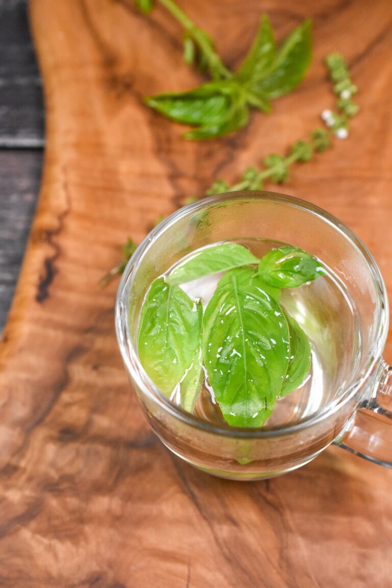 Fresh Basil tea in a clear glass mug on a wood cutting board with fresh basil in background