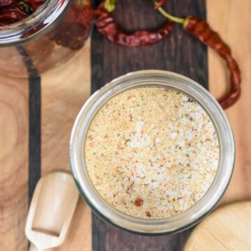 Homemade Fire Salt Recipe, SHown in a glass jar on a wood cutting board with dried peppers