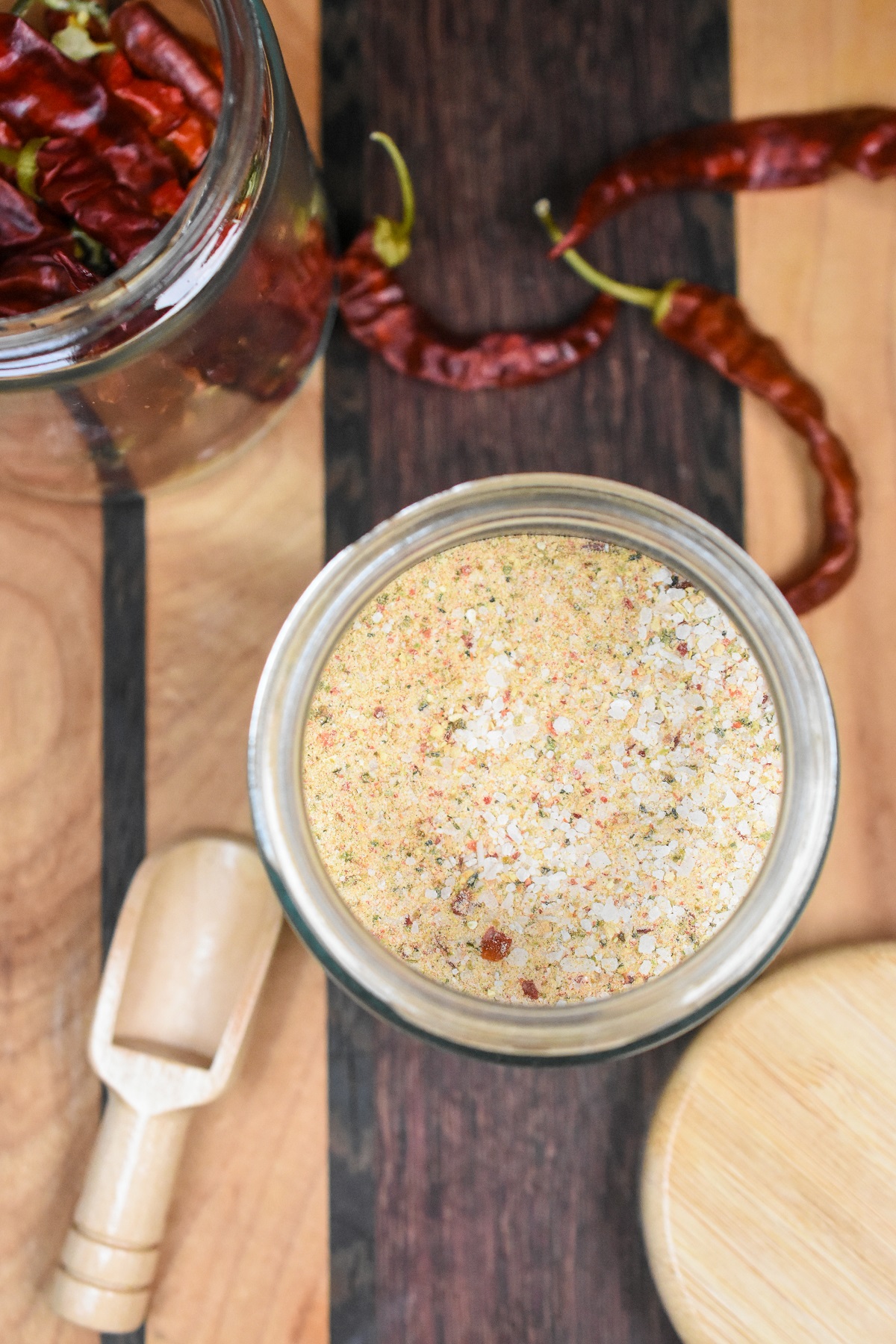 Homemade Fire Salt shown in a glass jar on a wood cutting board with a couple dried peppers visible.