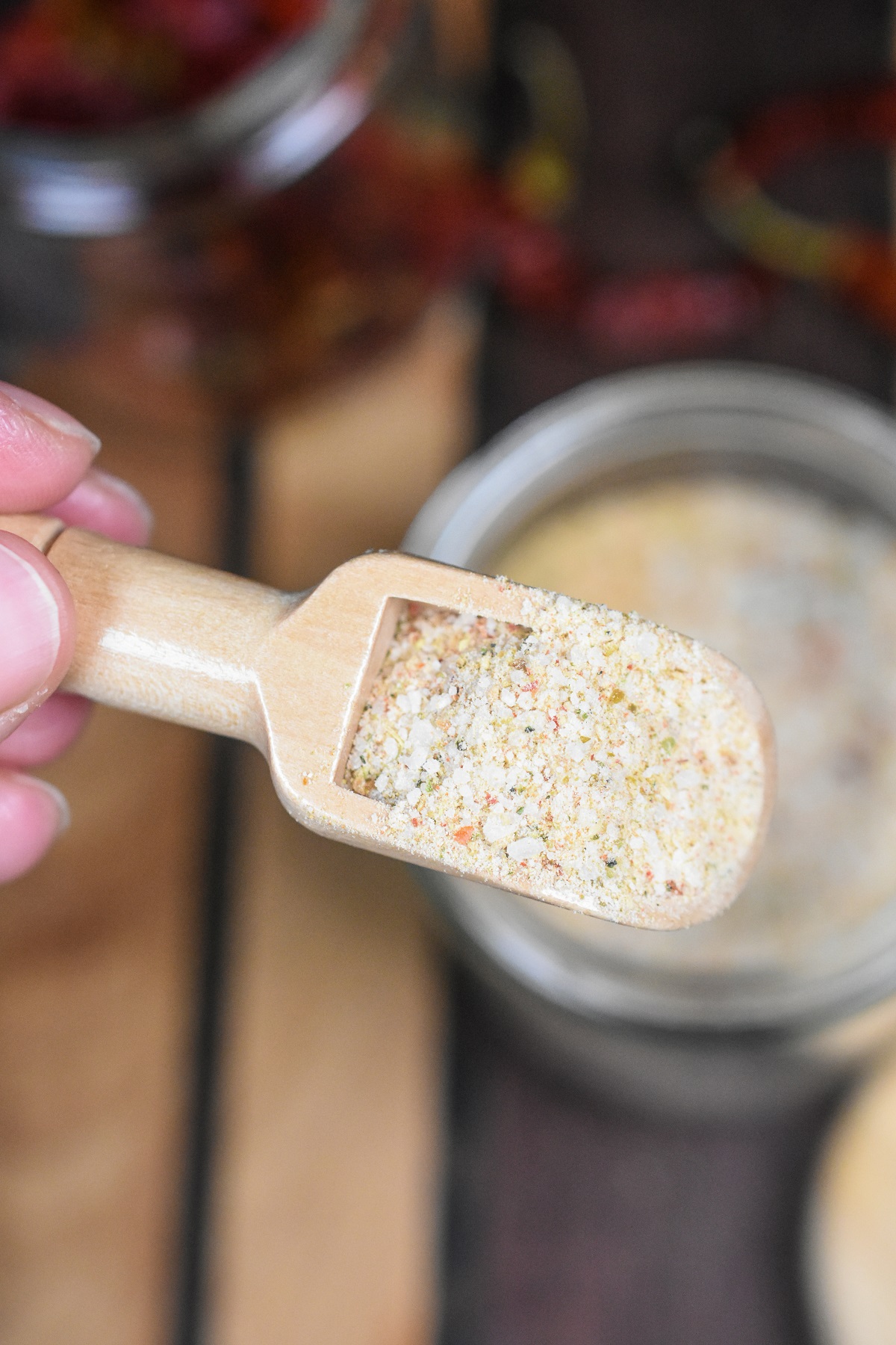 Homemade Fire Salt shown in a tiny wooden scoop held above a clear jar full of the fire salt