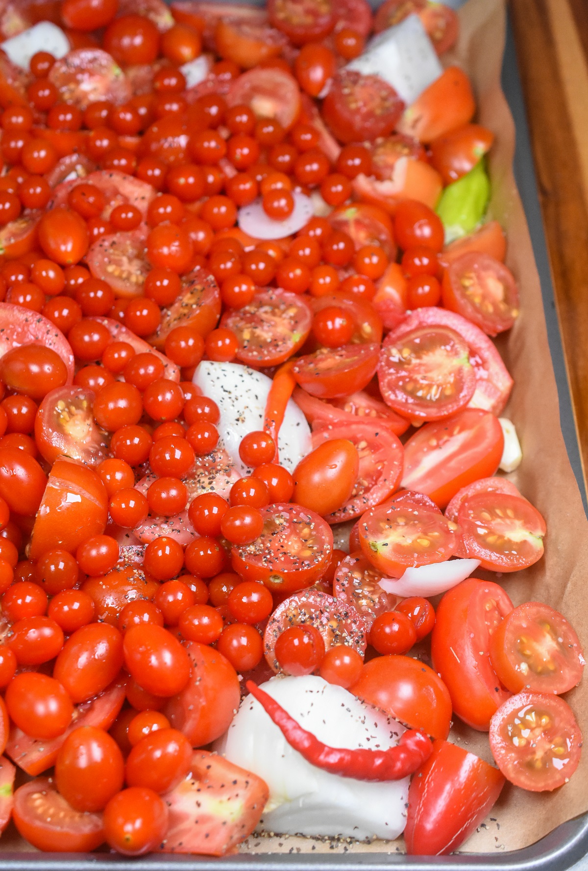Baking sheet tray full of raw tomatoes, onions, peppers and garlic ready to be roasted in oven.