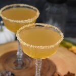 Apple Cider Martini shown 2 vintage martini glasses rimmed in caramel and sugar in the raw full with an apple cider martini on a wooden board