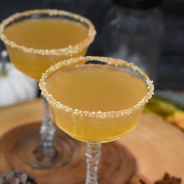 Apple Cider Martini shown 2 vintage martini glasses rimmed in caramel and sugar in the raw full with an apple cider martini on a wooden board