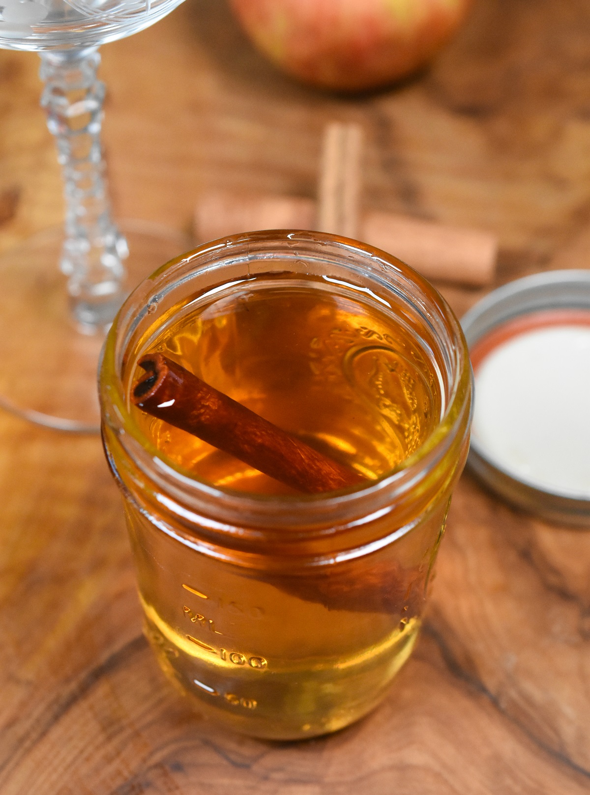 Homemade Cinnamon Syrup shown in an 8 oz mason jar on wood cutting board with a cinnamon stick floating the the jar.