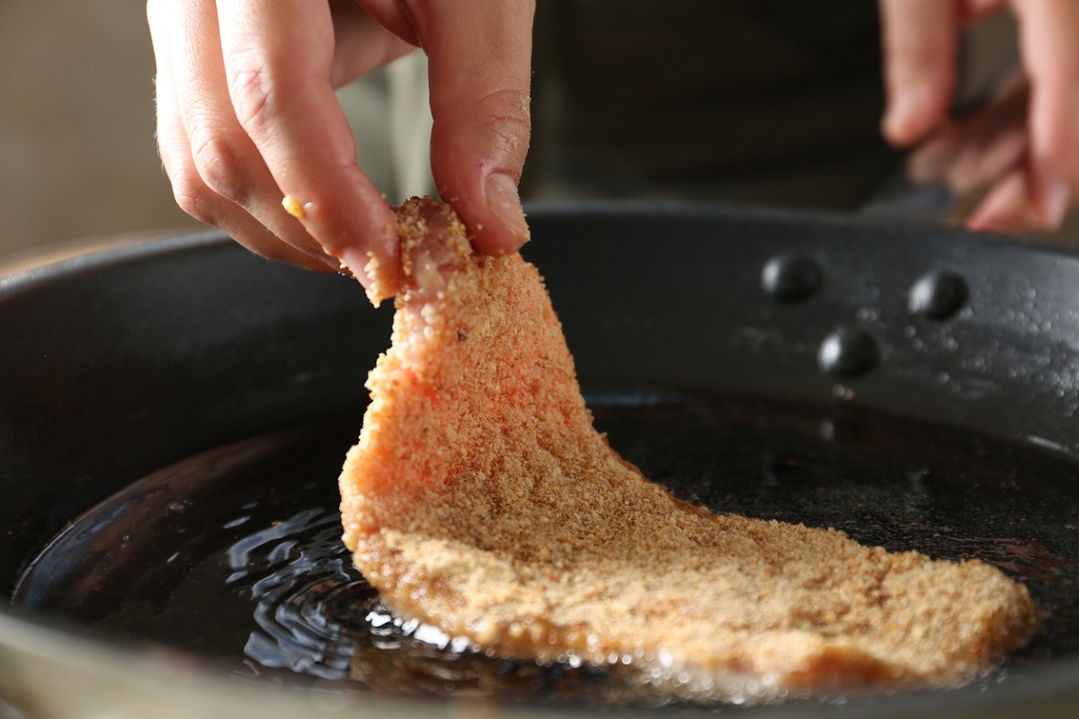 cooking a piece of Weiner Schnitzel. Placing breaded veal into the hot oil in a cast iron pan.