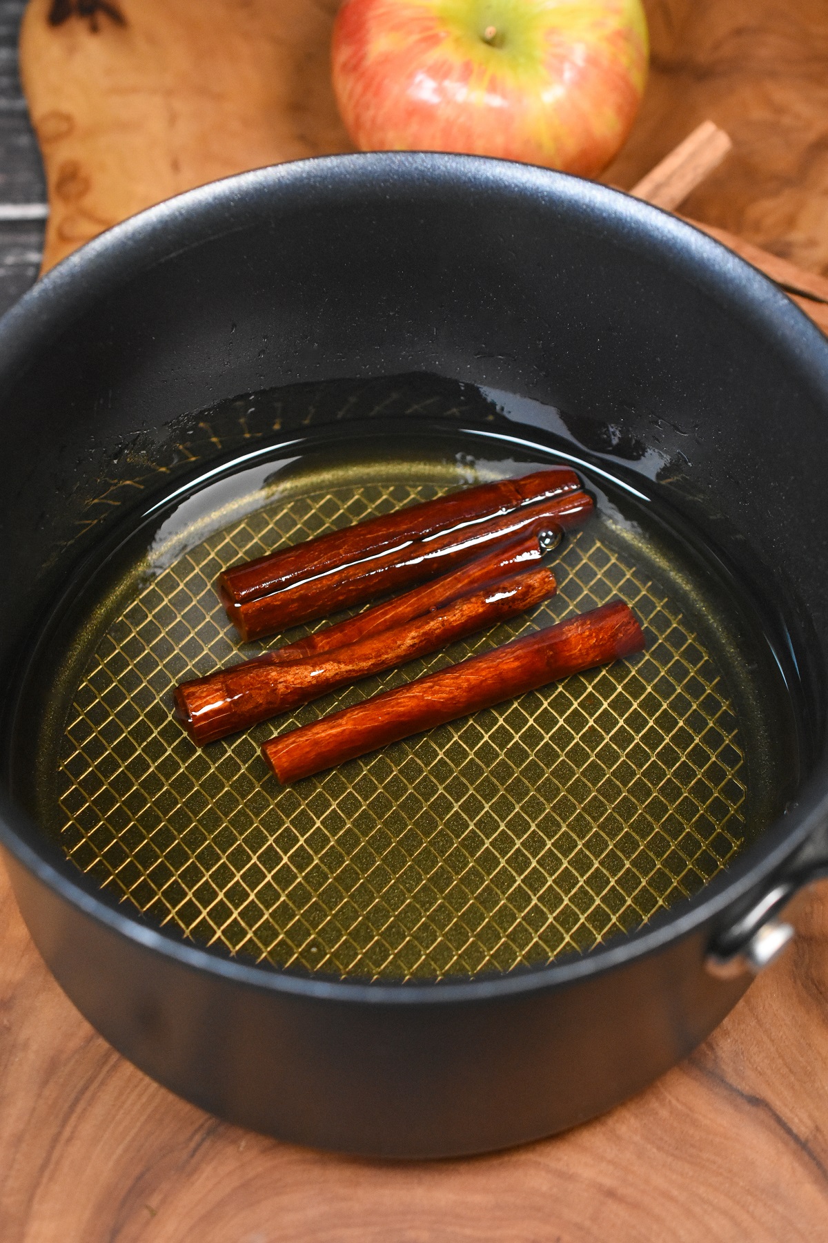 Easy Cinnamon Simple Syrup Recipe shown being made in an  pot. liquid in pot (the syrup cooling) three cinnamon sticks floating. Cinnamon Syrup.
