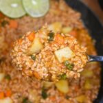 Picadillo shown cooked in a large cast iron pan, lime slices as garnish and a silver spook lifting some of the Picadillo up from the pan.