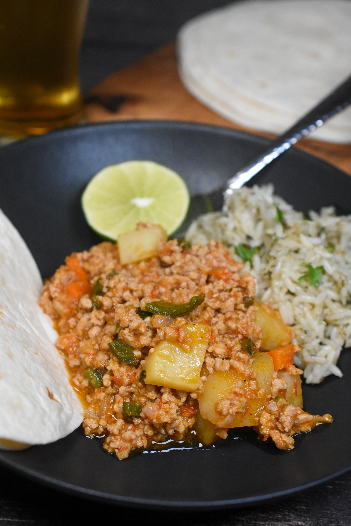 Picadillo made with ground veal on a black plate alongside flour tortilla and cilantro rice