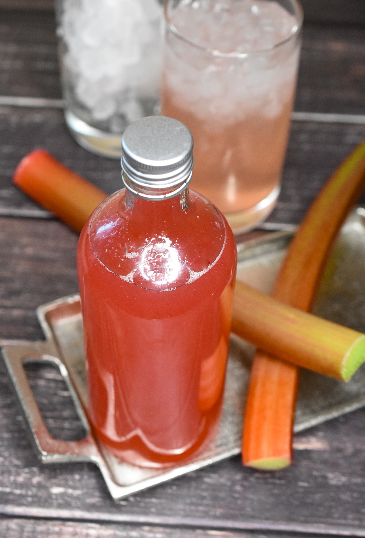 Easy Homemade Rhubarb Syrup recipe. Shown in glass bottle with 2 stalks fresh rhubarb below on a small silver tray.