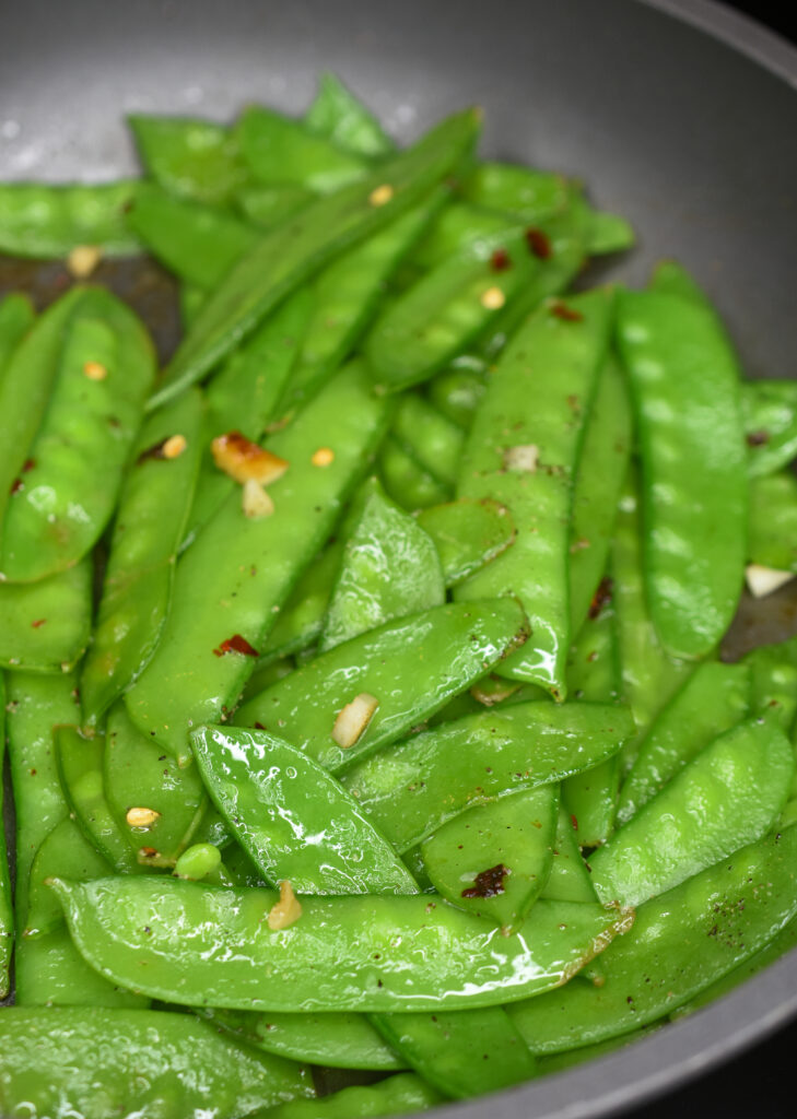 snow peas recipes shown sauteed snow peas in a grey pan cooked with garlic and red pepper flakes