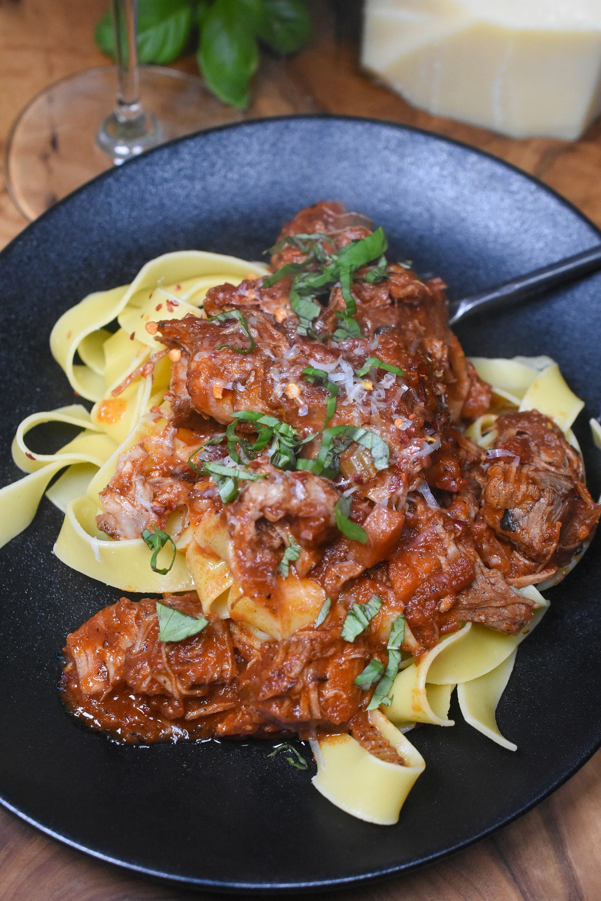 Ragout over pappardelle on a black plate garnished with basil 