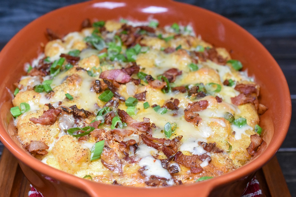 Tater Tot Breakfast Casserole.Shown in an orange baking dish. Garnished with scallions, bacon and cheese