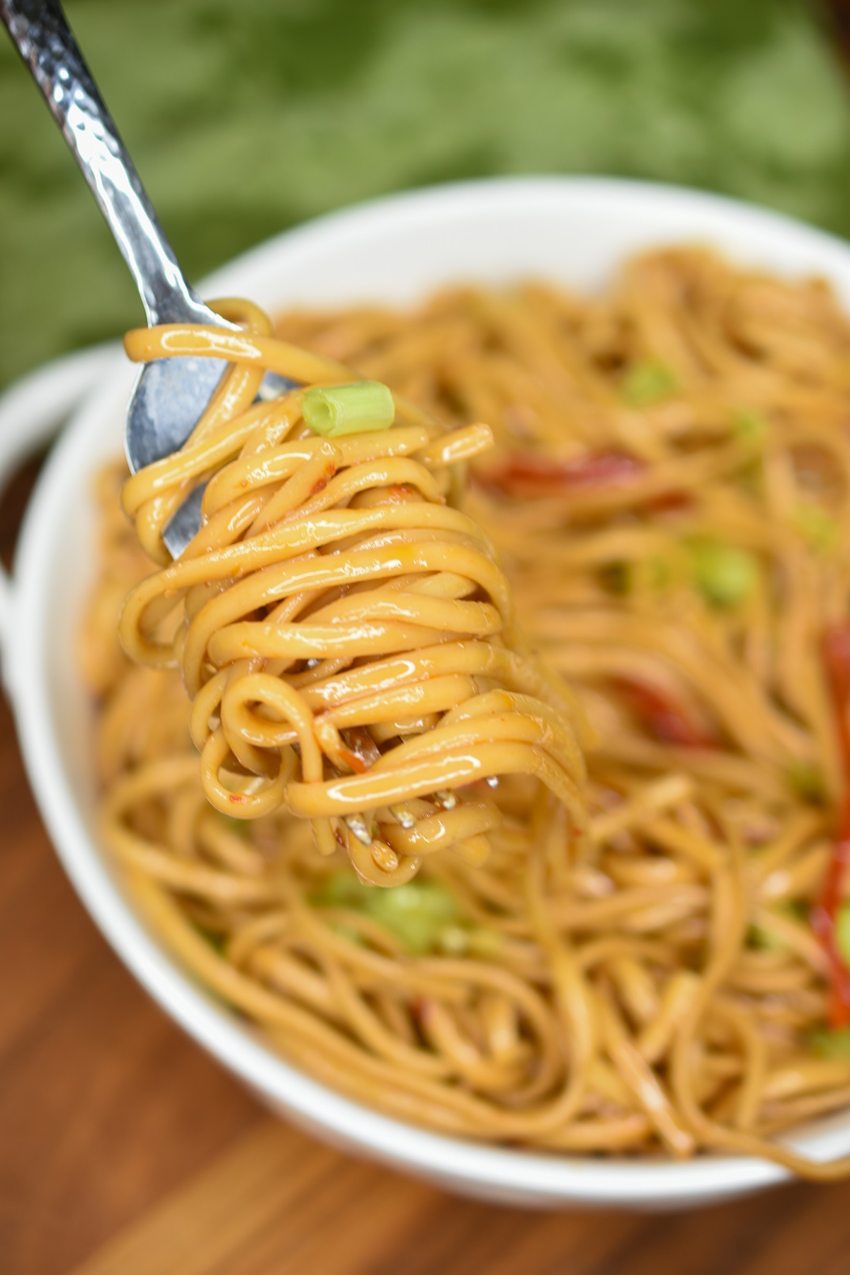 Asian Noodle Salad shown in white bowl with a fork twirling some of the noodles