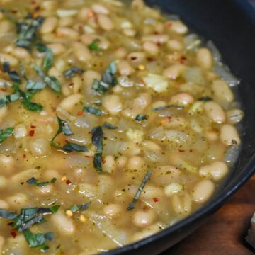 brothy beans in a pan with wilted spinach