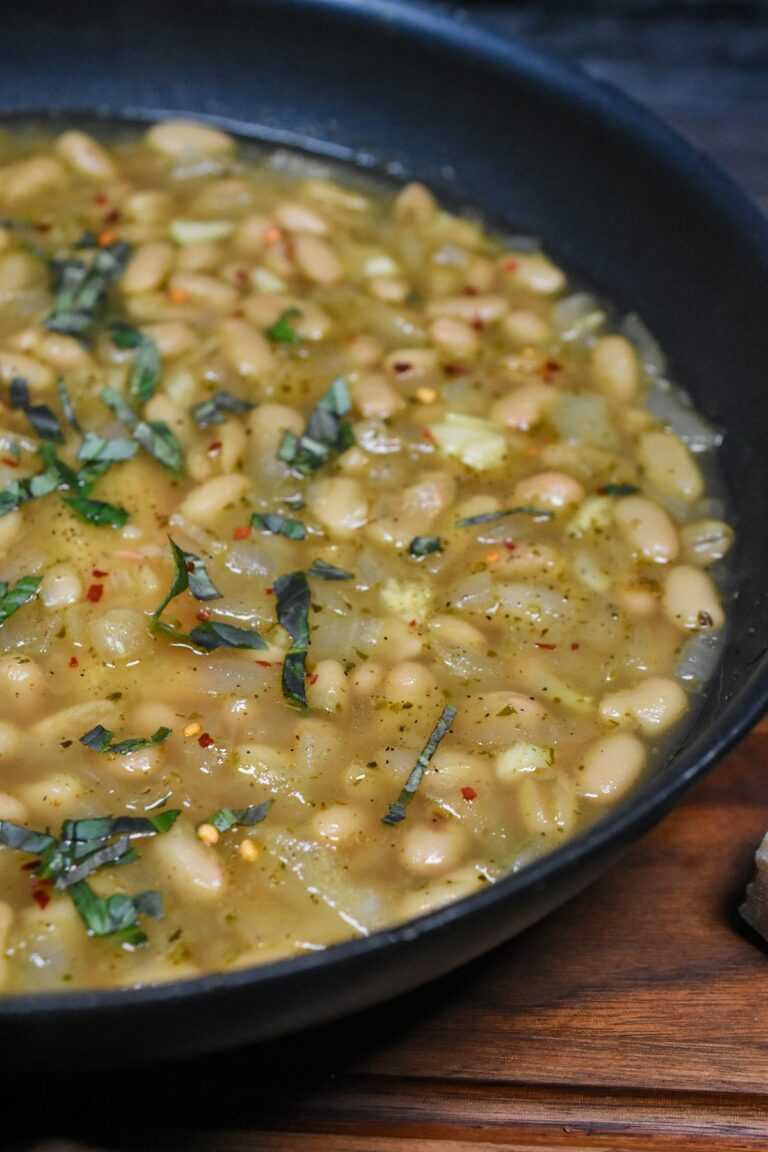brothy beans in a pan with wilted spinach