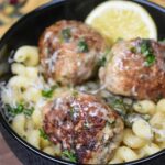 Three Chicken Piccata Meatballs in a black bowl over cavatappi pasta