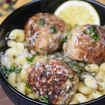 Three Chicken Piccata Meatballs in a black bowl over cavatappi pasta