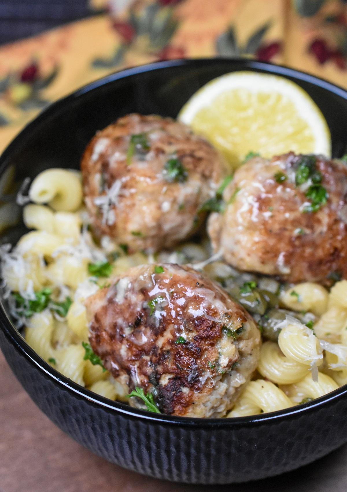Three Chicken Piccata Meatballs in a black bowl over cavatappi pasta