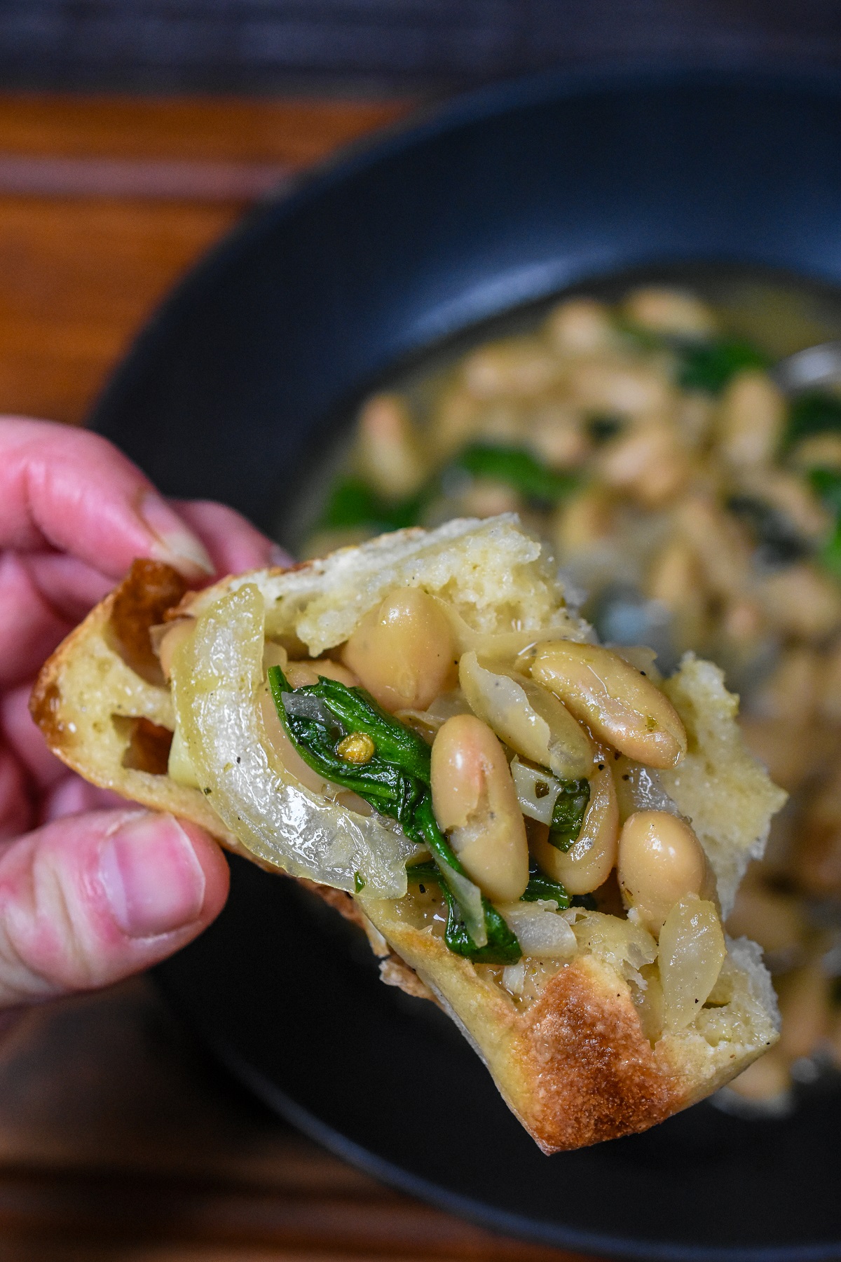 Brothy Beans recipe with spinach scooped up on crusty bread. Cannellini Beans Recipe