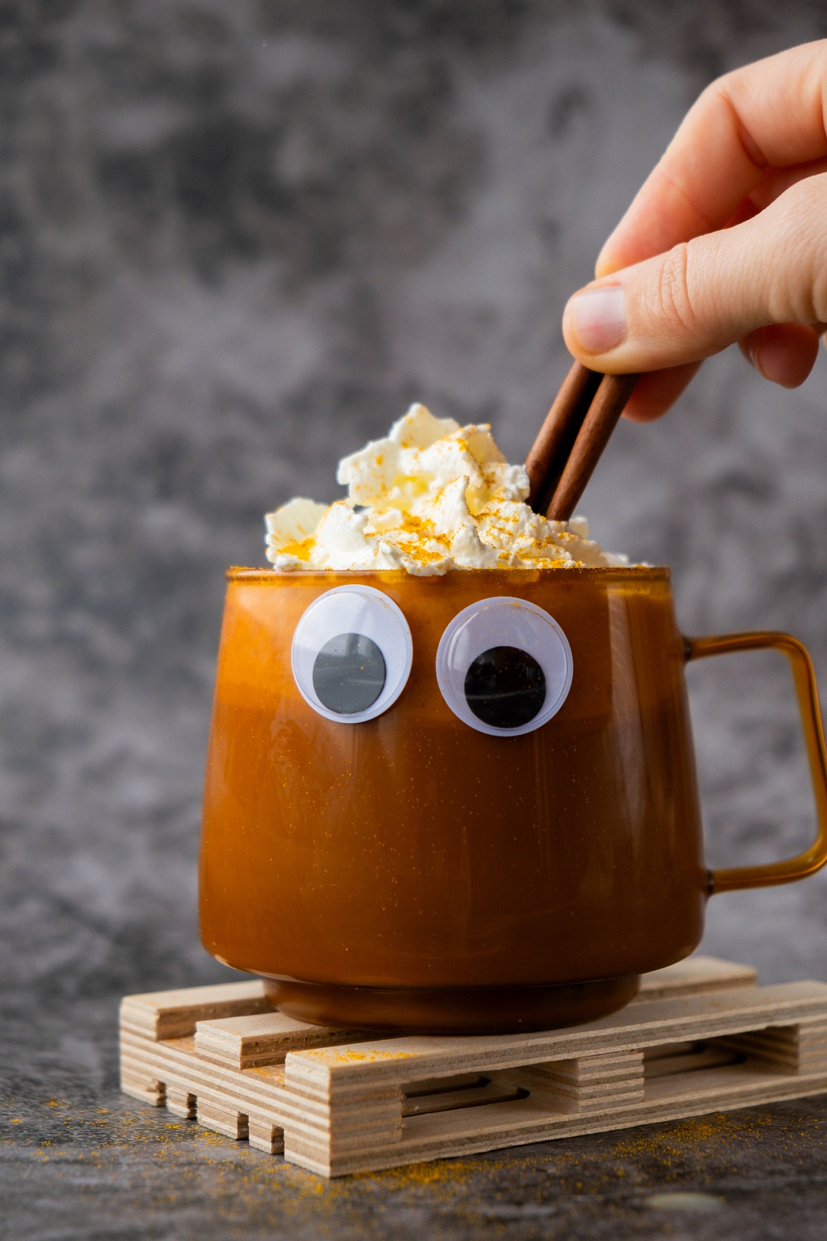 Fun way to decorate a drink for Halloween Halloween Drink Ideas. Sticky eyeballs on a brown mug of a hot caramel with cream and cinnamon stick.