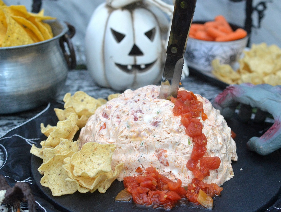 Halloween Brain Dip! Taco dip in the shape of a brain using a mold. garnished with a knife sticking out of it and a trail of "blood using diced tomatoes.