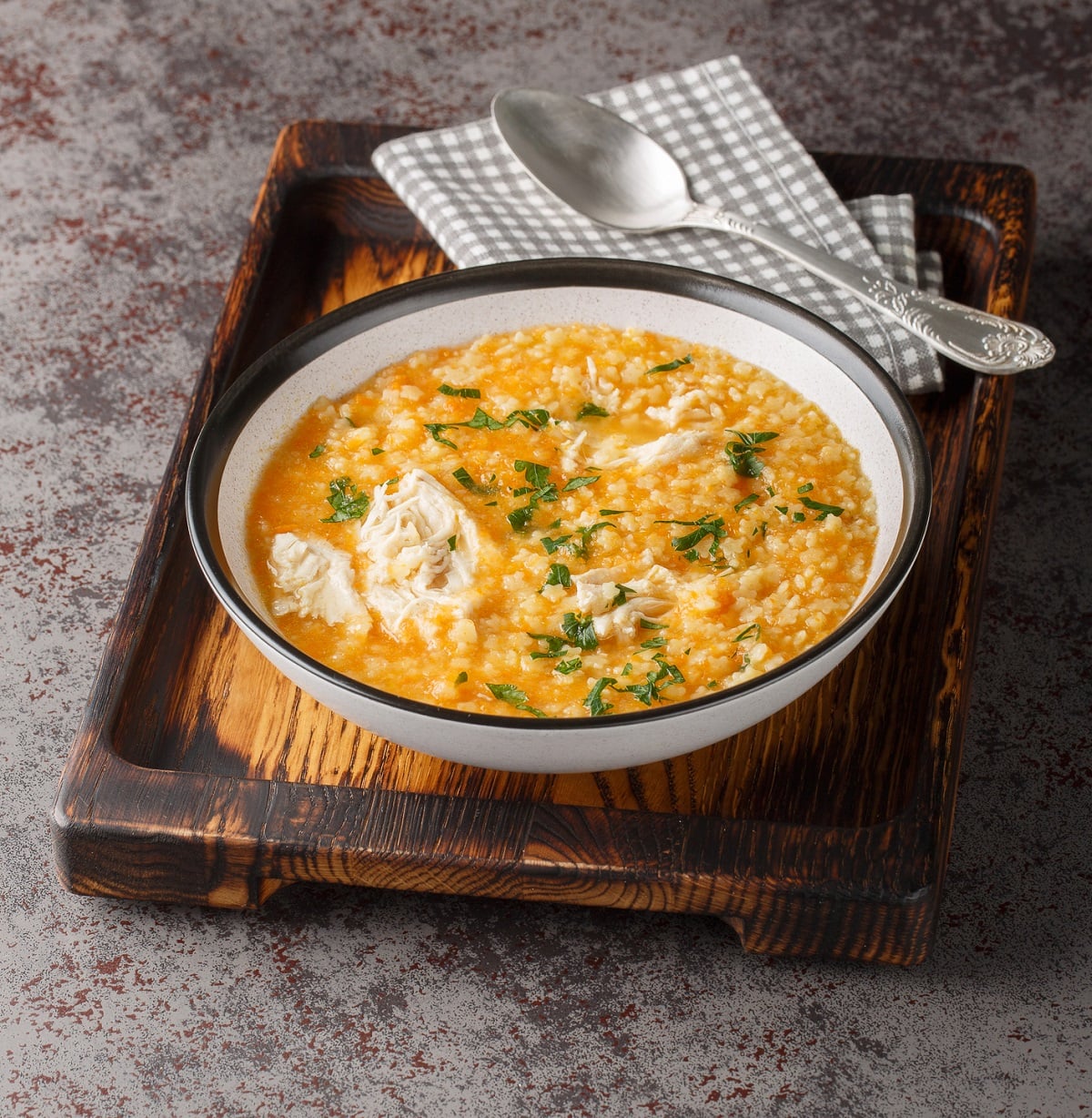 Bowl of chicken pastina soup with shredded chicken on a wood tray with a spoon and grey checkered napkin